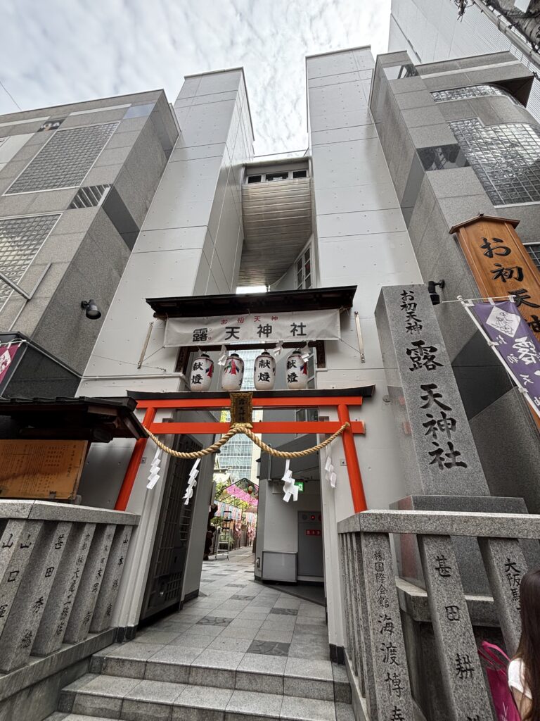 朱塗りの鳥居と「お初天神 露天神社」の横断幕。ビルに挟まれたお初天神の入口