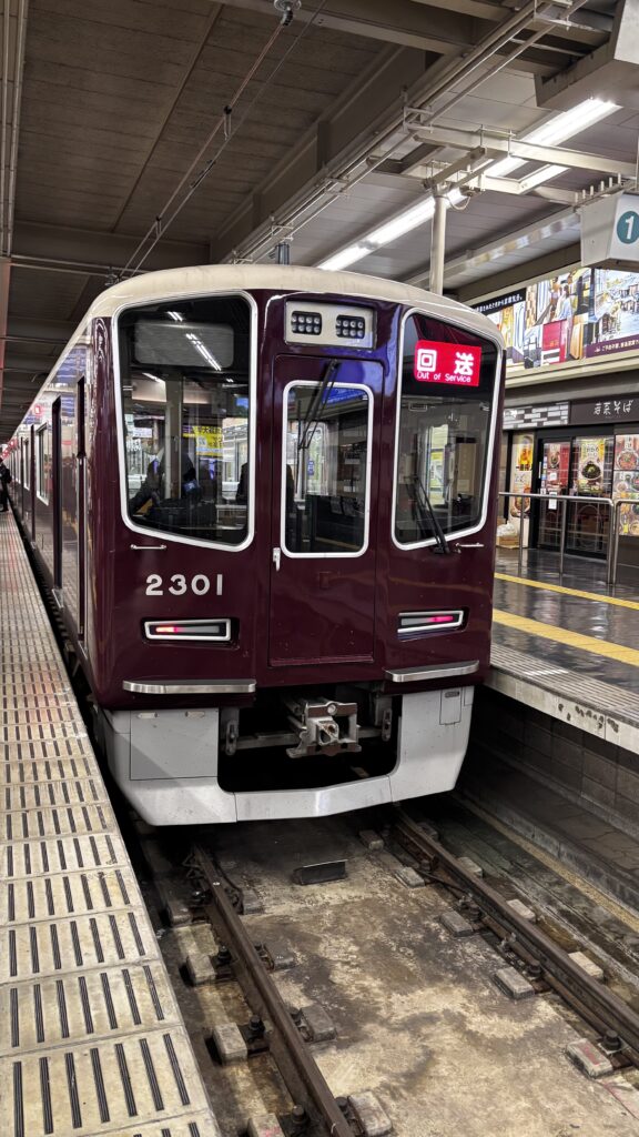 A maroon Hankyu 2300 series at the platform, its indicator reading "Out of Service"