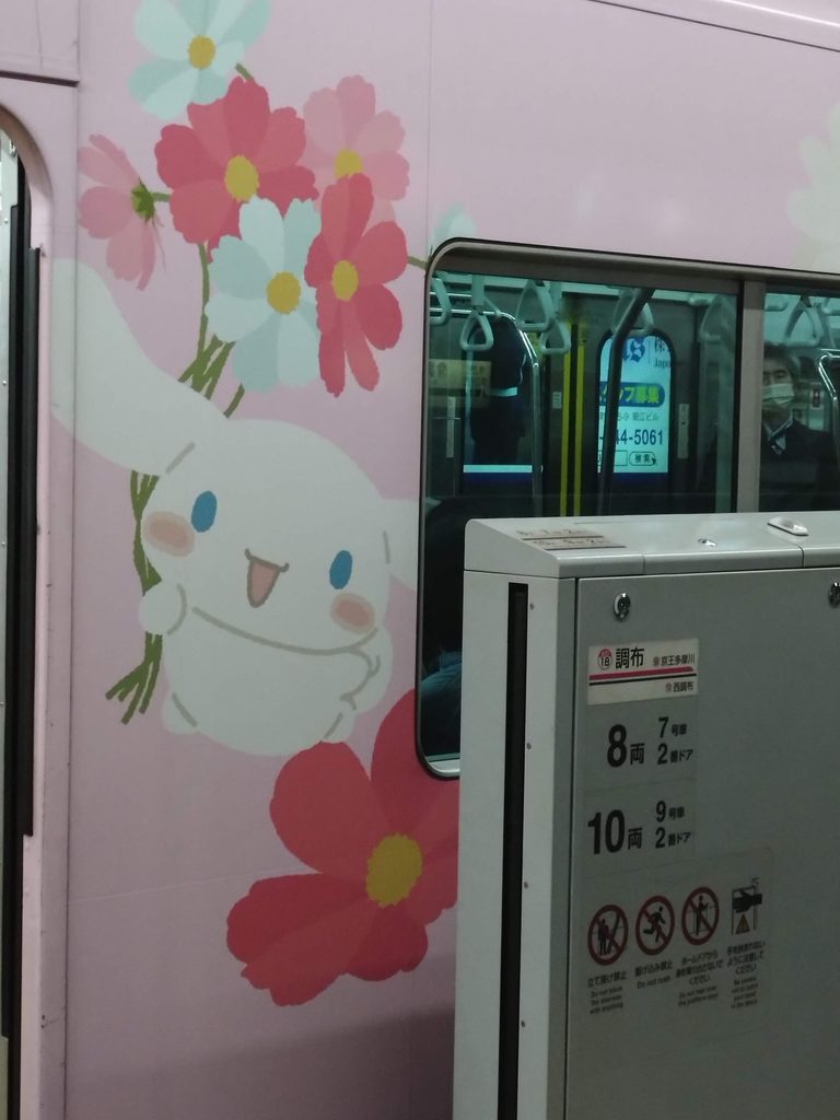 The Sanrio wrapped train seen over the platform doors at Chofu station, with Cinnamoroll holding cosmos flowers