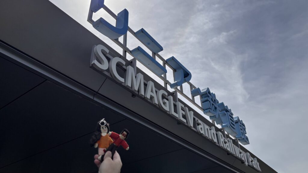 「SCMAGLEV and Railway Park／リニア・鉄道館」の看板を見上げるマスコットのTikoppiとプレスリー